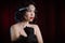 Old-fashioned woman dressed in style of Flappers posing on dark red background. Roaring twenties, retro, party, fashion