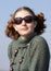 Old-fashioned Young curly girl in a vintage gray knitted dress in sunglasses.