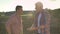 Old father and son talking, dad holding soil on palm and talking, standing on ground in field, sunset and beautiful