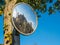 Old flyblown convex glass road safety mirror over tree with house reflection in english village