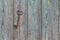 An old forged beautiful rusty key hangs on an old iron nail on a wooden wall, with peeling paint