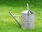 Old galvanized watering can on green lawn.