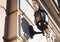 Old glass lantern in a black twisted frame on the white wall of the city building. Wall lamp on a Sunny day