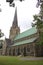 Old Gothic brown and gray roof church taken behind trees in a cloudy summer weather with a beautiful green lawn.