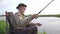 Old grandfather in a hat enjoying fishing on the beautiful lake.