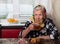 Old grandmother sits with cookies and sweets at a table in her village hut and drinks tea