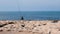 Old gray-haired fisherman in dark sweater and cap with fishing rod sitting on seashore and catching fish