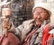 Old gray-haired ladakhi man with glasses and hand prayer wheel in traditional clothes and knitted hat