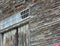 Old gray siding of old wooden barn peeling aound transom window above barn doors