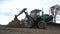 Old green excavator is digging a hole at a construction site, heavy machinery