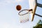 Old grunge basketball falling into old grunge basket and backboard on blurred sky background
