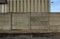 Old grunge concrete surrounding wall in front of an industrial building made of cement blocks. Weathered asphalt road in front.