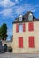 Old historical building with red window shutters and outdoor decor. Empty street in village, France. Facade of ancient house.