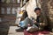 Old homeless man sitting on cardboard holding bowl with food in hand.