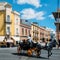 Old horse drawn carriage carrying tourist passsengers with vibrant Spanish architecture in background