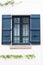 Old house beige wall with window with opened dark blue gray wooden shutters with metal grilles.