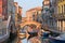 Old houses, moored boats and pedestrian bridge across canal in Venice, Italy. Tourists are returning to Venice, but far