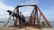 Old huge abandoned railway rusty bridge above water. Coast. Summer. Zoom in.