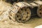 Old iron caterpillar in wet sand. Rusty steel wheels and caterpillar tape of a large bulldozer, tank, excavator, in damp sand and