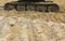 Old iron caterpillar in wet sand. Rusty steel wheels and caterpillar tape of a large bulldozer, tank, excavator, in damp sand and