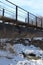 Old, iron rusty pedestrian bridge over the river in a ravine dangerous technical crossing in winter in the snow over the heating