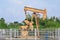 Old isolated rusty oil pump jack extracting crude oil and natural gas form well in green and cloudy oil fields of India, Asia