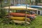 A old kayaks and canoes lie on the open-air rack. yellow orange blue red plastic boats