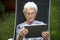 old lady sitting on a lounge chair reading from a tablet in the garden of her house