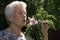 old lady smelling a pink flower in the garden of her house