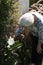 old lady smelling a white flower in the garden of her house