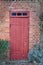 An old, large, red wooden door in a face brick building, most likely a house in a residential district. The entrance way