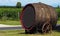 Old large wine barrel tilted to the side with wooden wheels in front of a vineyard. It is used as decoration and signpost .