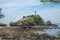 An old lighthouse on top of a cliff near a rocky shore. The rock is covered with greenery. Beautiful seascape from Koh Lanta