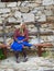 Old local woman sitting on a bench in front of stone wall on the street of the historical town and ethnographic reserve of