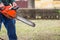 Old man in blue pants hold orange chainsaw with his bare hands