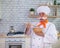 An old man with a bushy gray mustache in a chef's hat is cooking in the kitchen.