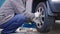 old man in dirty pants removing tire of silver car at cloudy autumn day