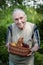 Old man holds a basket with a crop of apricots and cherries. A gray-haired old man is working in the garden, harvesting