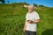 Old man keeping cellphone, standing on field looking at side.