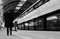 Old man walking with his head down along an train on an empty platform in black and white