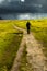 Old Man With Walking Stick Strolls On Narrow Gravel Path Through Scenic Landscape With Spectacular Clouds