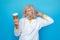 Old man wearing doctor`s gown studio isolated on blue standing looking at cup of coffee smiling confused