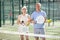 Old man and woman posing with Padel racket in hands next to the net in tennis court