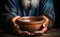 Old mans hands clasp empty bowl on wood, conveying the plight of poverty