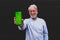 Old and mature man holding his smartphone showing it at the camera with the green screen - smiling happy adult portrait using