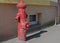 Old metal fire hydrant of cylindrical shape, painted in red, standing on the concrete pavement of an old apartment building