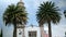 Old Mexican church entrance surrounded by bushes and two palm trees