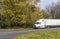 Old model used big rig semi truck with shabby semi trailer driving on autumn road with yellow and green trees