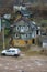 An old multi-storey wooden house in a poor area. A white car is parked near the cottage. Poor living conditions in impoverished