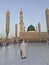 An old Muslim man walks towards masjid Al Nabawi minaret and green dome in Madinah, Saudi Arabia